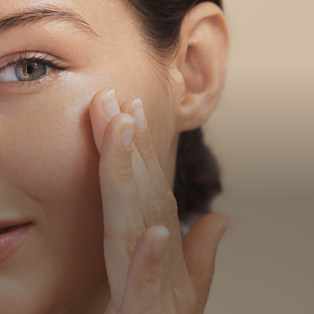A woman pressing Nimi moisturizer into her cheek with her fingertips