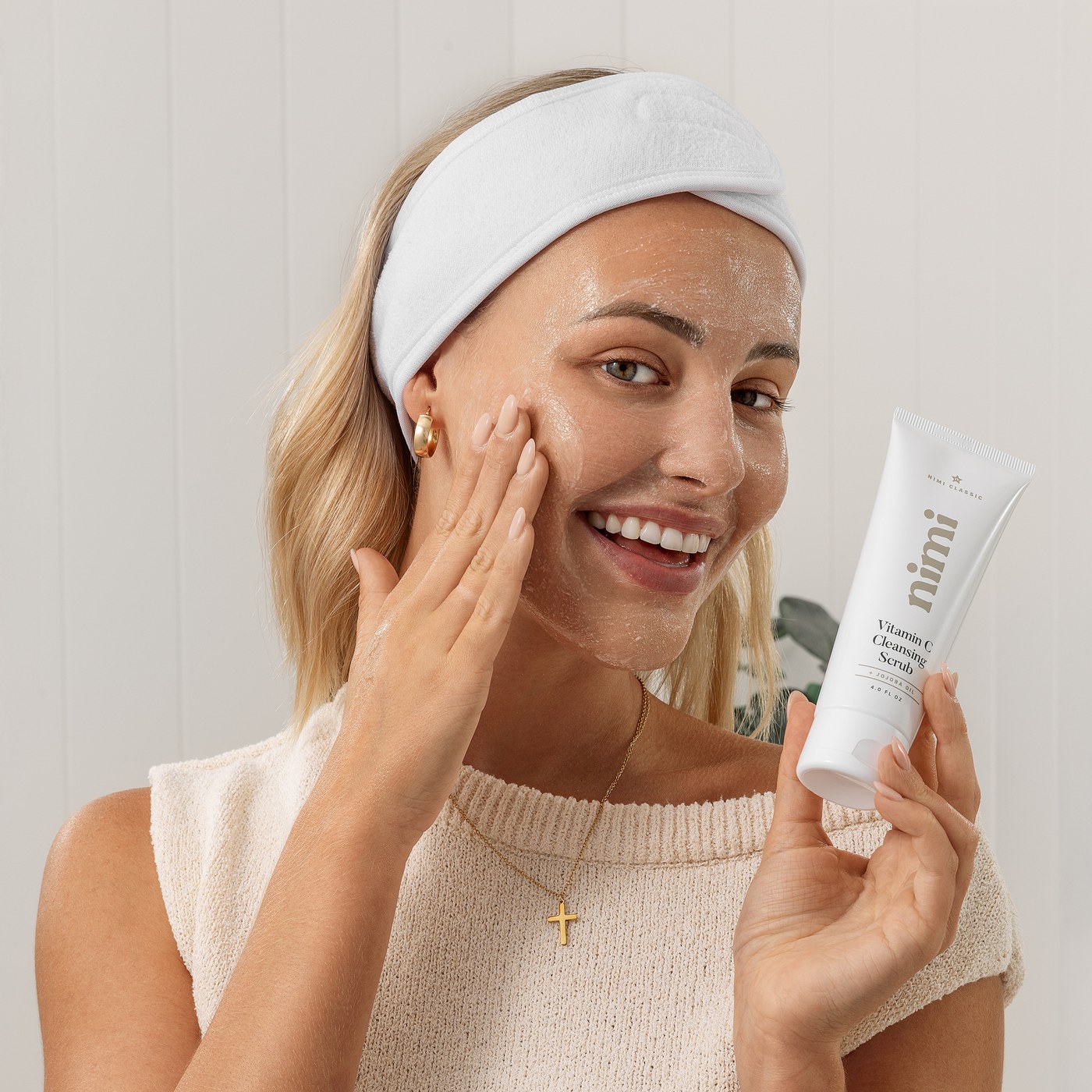 A woman in a spa headband applying the Nimi Vitamin C Cleansing Scrub to her cheek