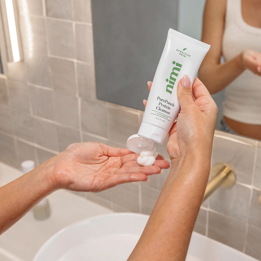 Hands squeezing Nimi PurePunch Protein Cleanser into a cupped palm at a tiled bathroom sink